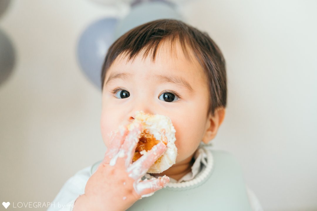 スマッシュケーキをする赤ちゃんのアップ写真。自分の右手で口にケーキを押し付け、手や口の周りにはクリームが付いている。