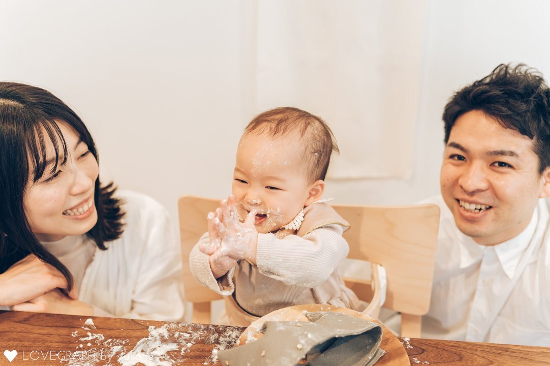 スマッシュケーキを楽しむ赤ちゃんを両親が見守って笑っている幸福感のある写真