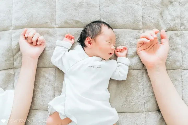 大人の両腕の間にすっぽりと収まって眠る、白い産着を着た小さな赤ちゃん。ご両親の愛情に包まれているような温かい雰囲気の写真
