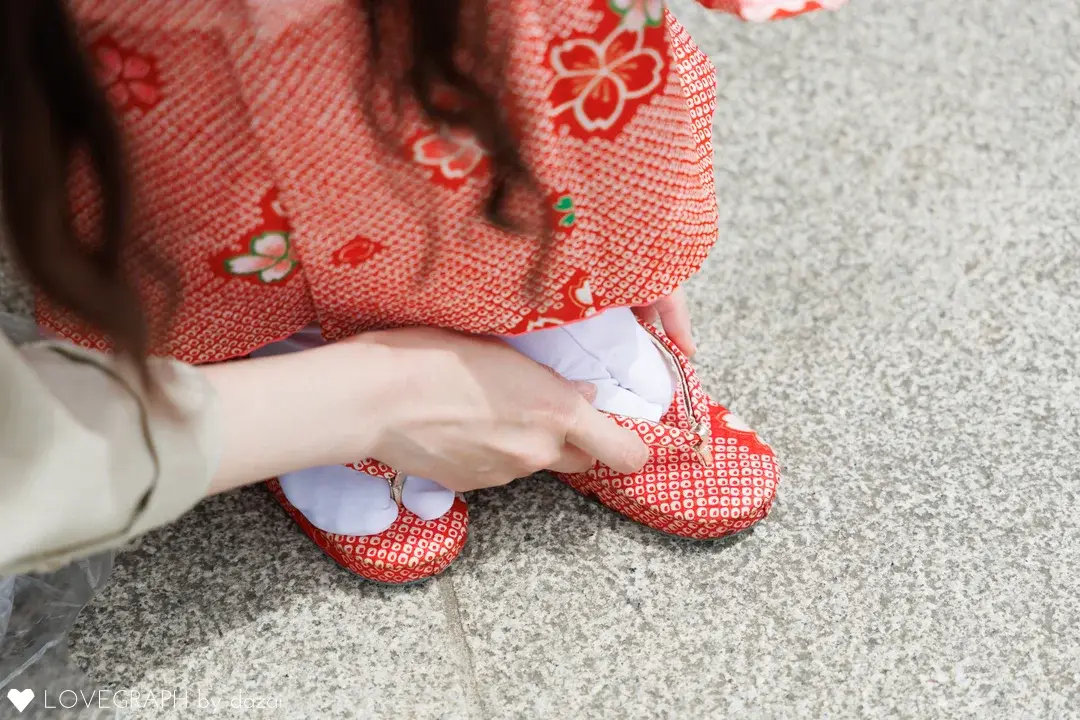 大人が子どもの足に赤い草履を履かせている手元の写真。子どもは赤い鹿の子模様に桜柄の着物と白い足袋を身につけている。