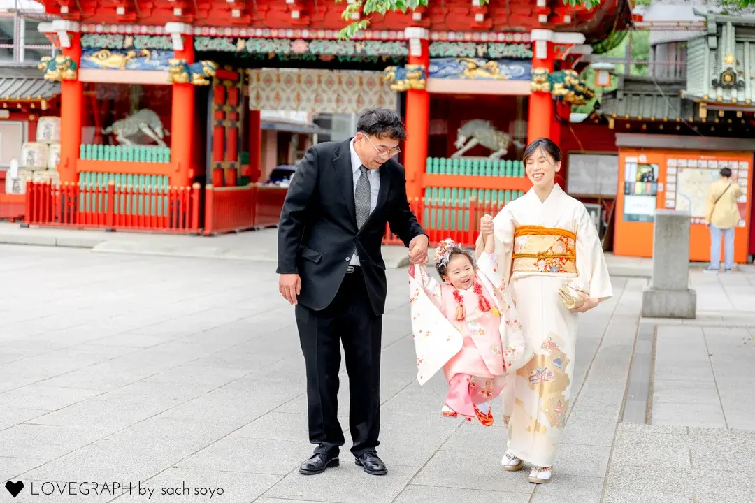 神田明神の隨神門を背景に、スーツ姿の父親と和装の母親の手を握って楽しそうにはしゃぐ3歳女の子の七五三出張撮影