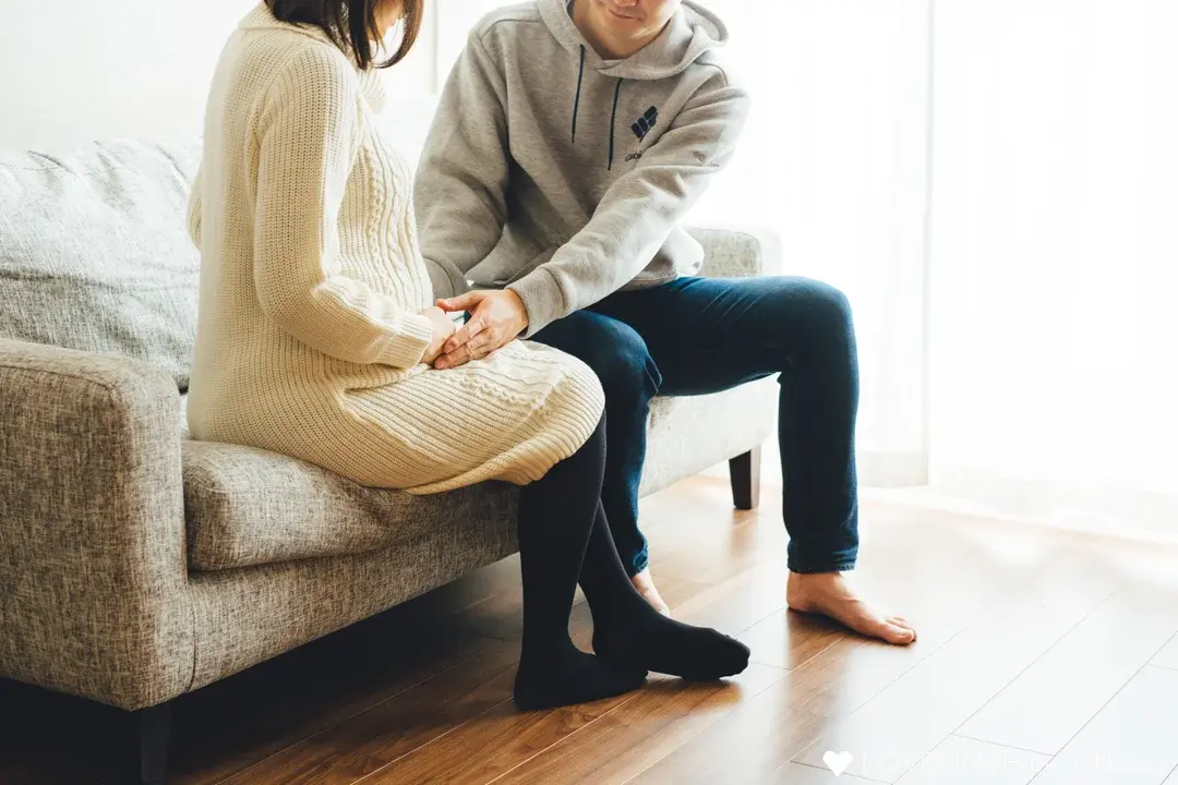 ソファに並んで座り、ふたりで大きなお腹に手を添える妊娠中の女性と男性