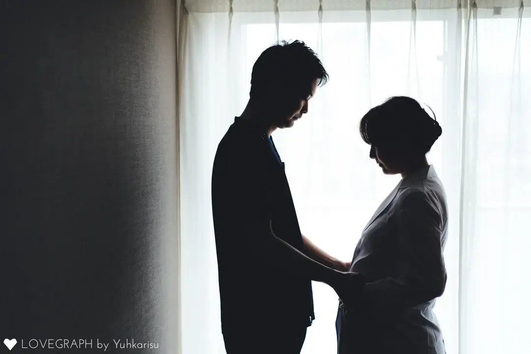 窓際で静かに向かい合い、生まれてくる命を愛おしむようにふたりでお腹に手を添える、ドラマチックなマタニティフォト